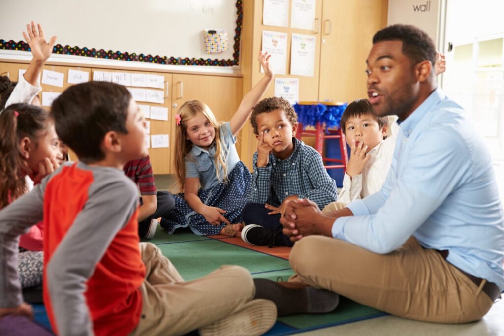 Image of Elementary school kids and teacher sit cross legged on floor