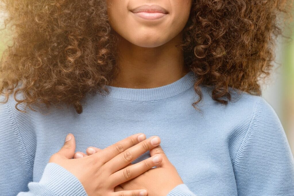 Image of African american woman wearing a sweater smiling with hands on chest with closed eyes and grateful gesture on face.