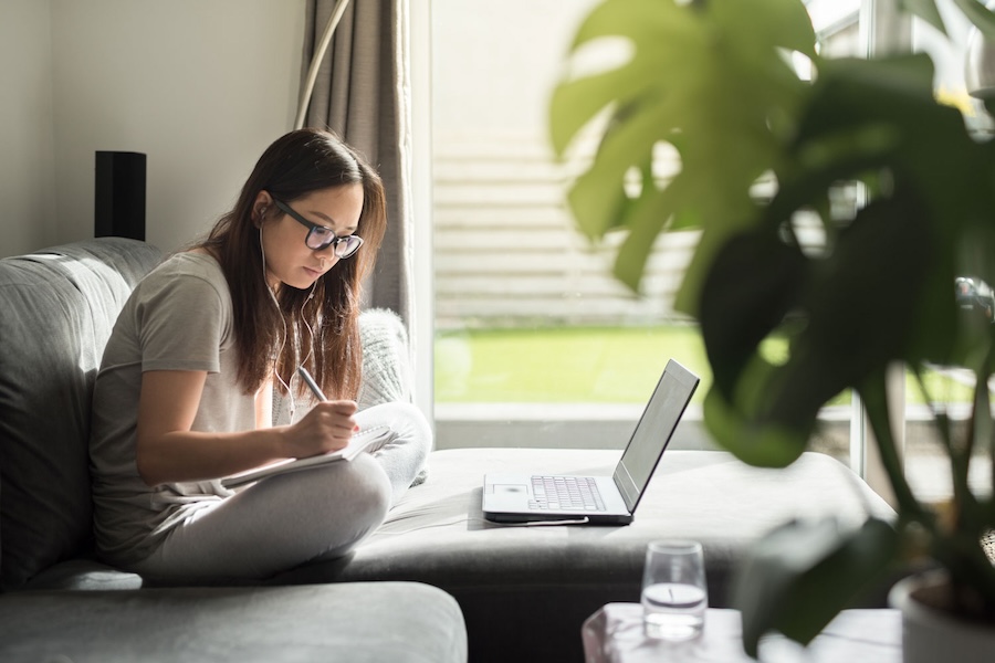 A young woman sitting on a couch doing work with headphones in.