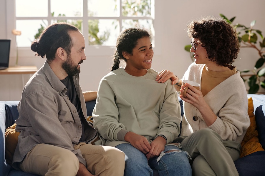 Image of a mother and father sitting between a girl on a couch