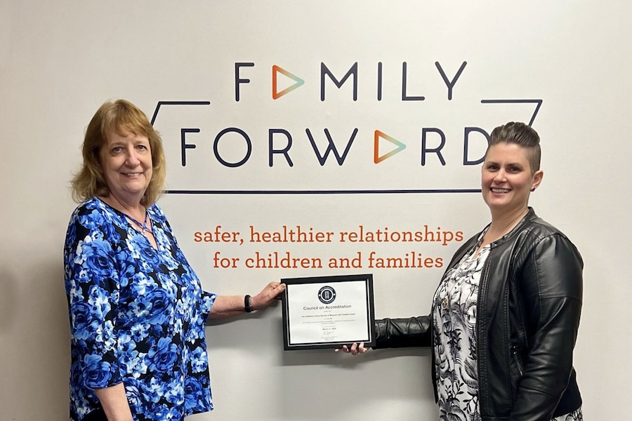 Image of Two women holding up a plaque while standing under a Family Forward sign