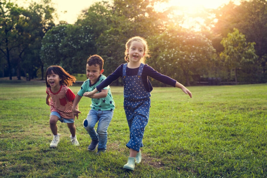 3 kids hold hands while running and playing in a field