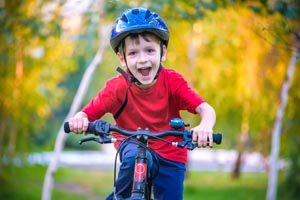 Happy kid boy of 6 years having fun in autumn forest with a bicycle on beautiful fall day. Active child making sports. Safety, sports, leisure with kids concept.