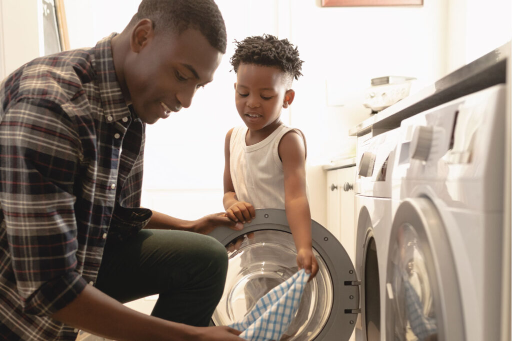 A young man doing laundry with a young child.