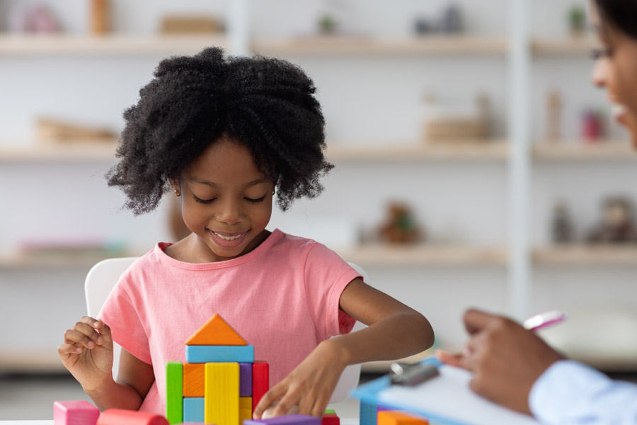 A young girl playing with blocks as therapist observes her.