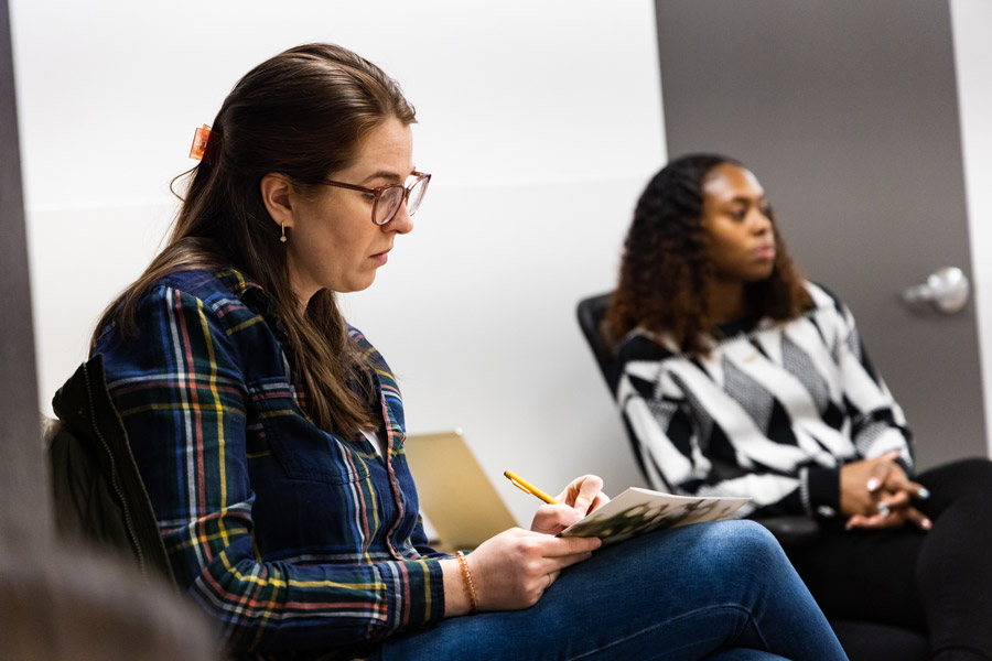 Two women sitting down in a room. One woman is writing on a piece of paper.