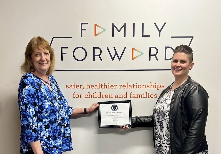 Image of Two women holding up a plaque while standing under a Family Forward sign