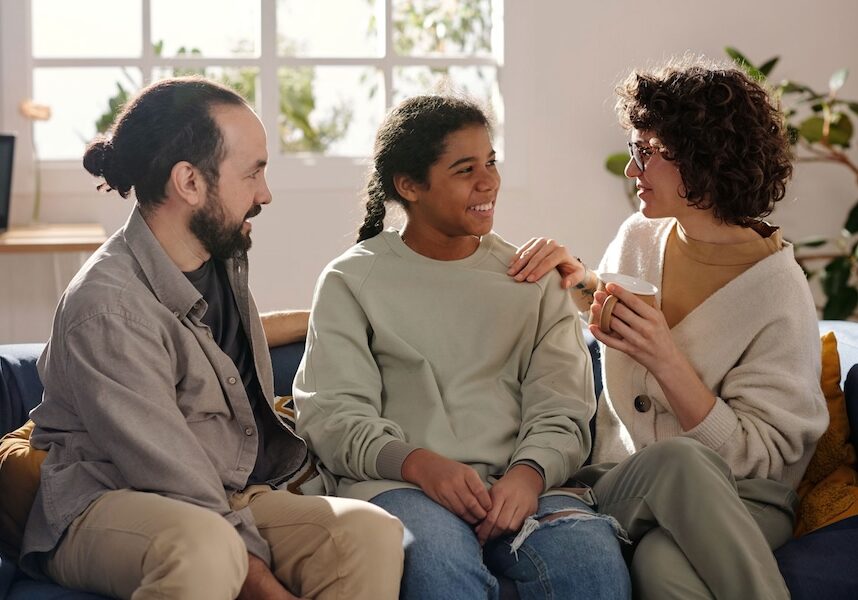 Image of a mother and father sitting between a girl on a couch