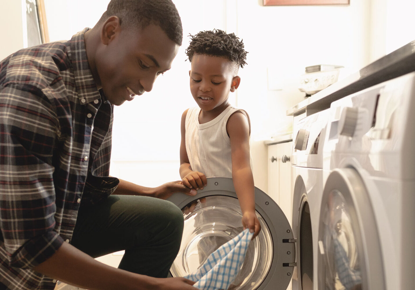 A young man doing laundry with a young child.