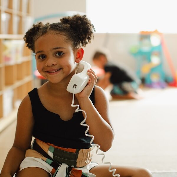 Image of a young girl holding a play phone to her ear and smiling