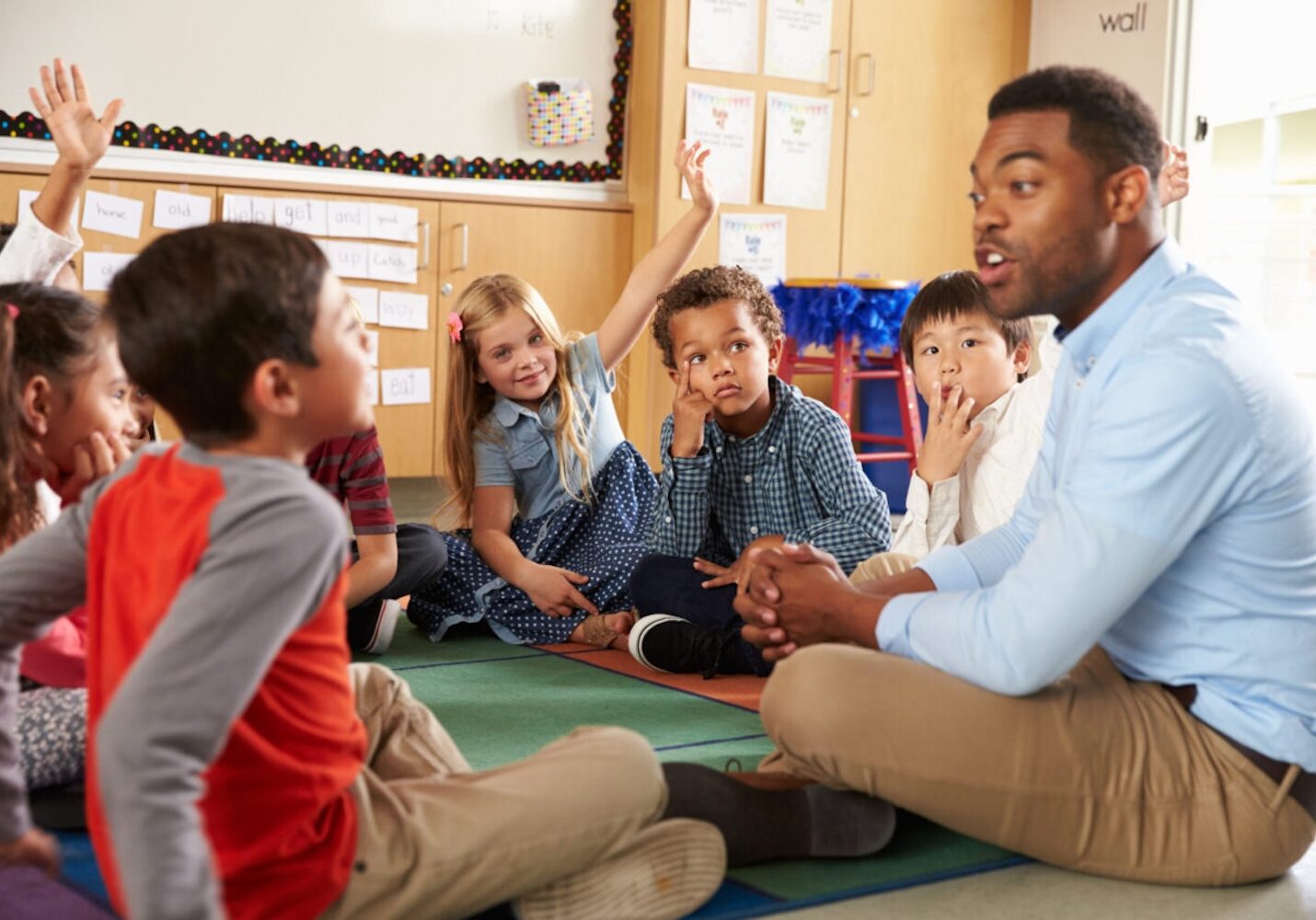 Image of Elementary school kids and teacher sit cross legged on floor