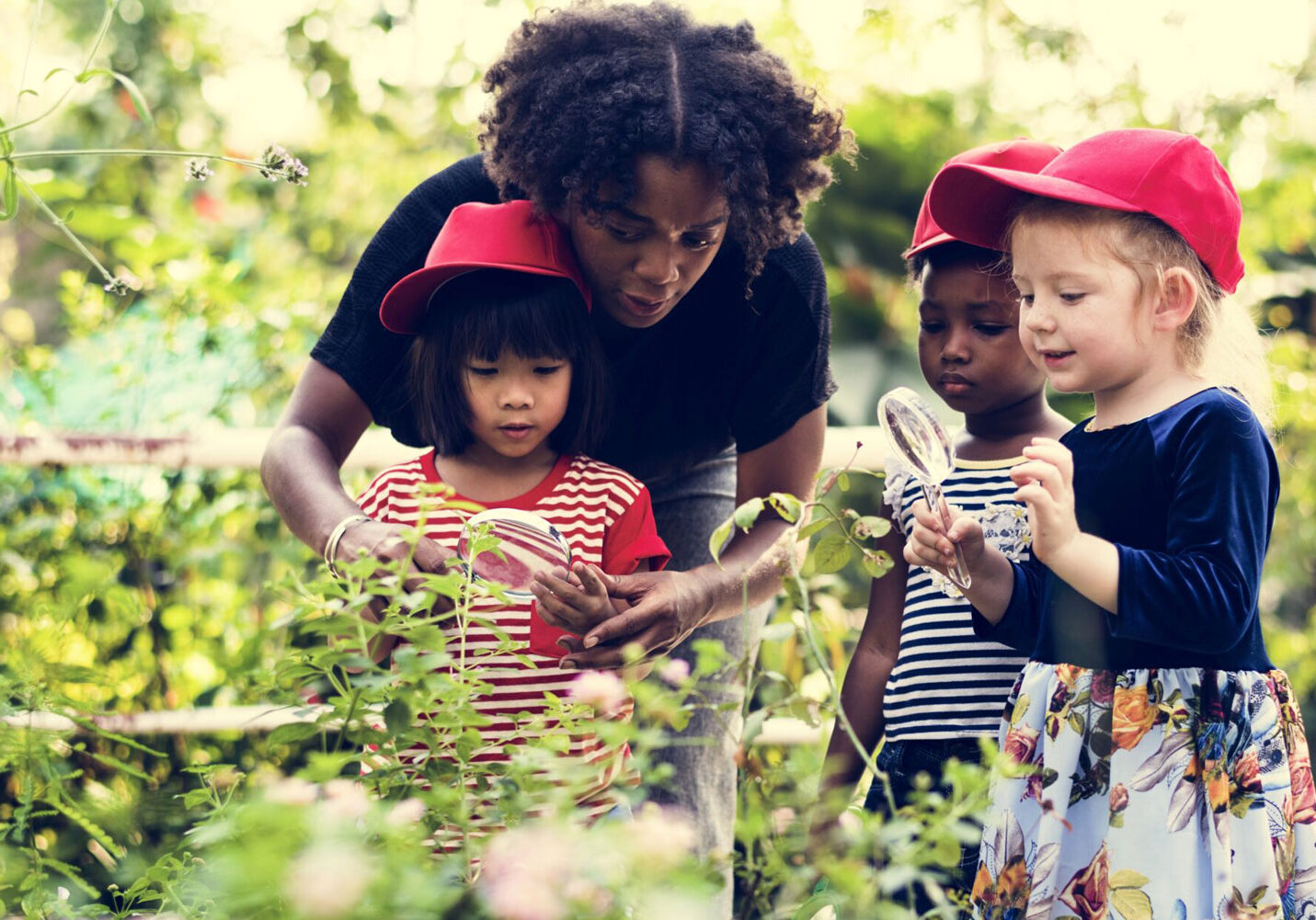 A woman and three children outside in a gardening looking at plants with magnified glasses.