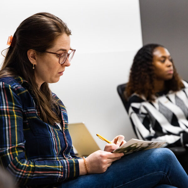 Two women sitting down in a room. One woman is writing on a piece of paper.