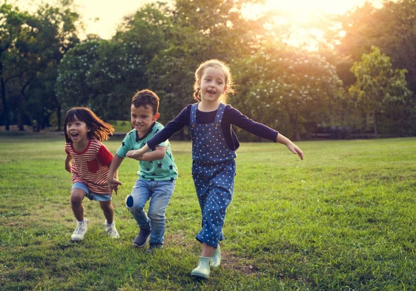 3 kids hold hands while running and playing in a field